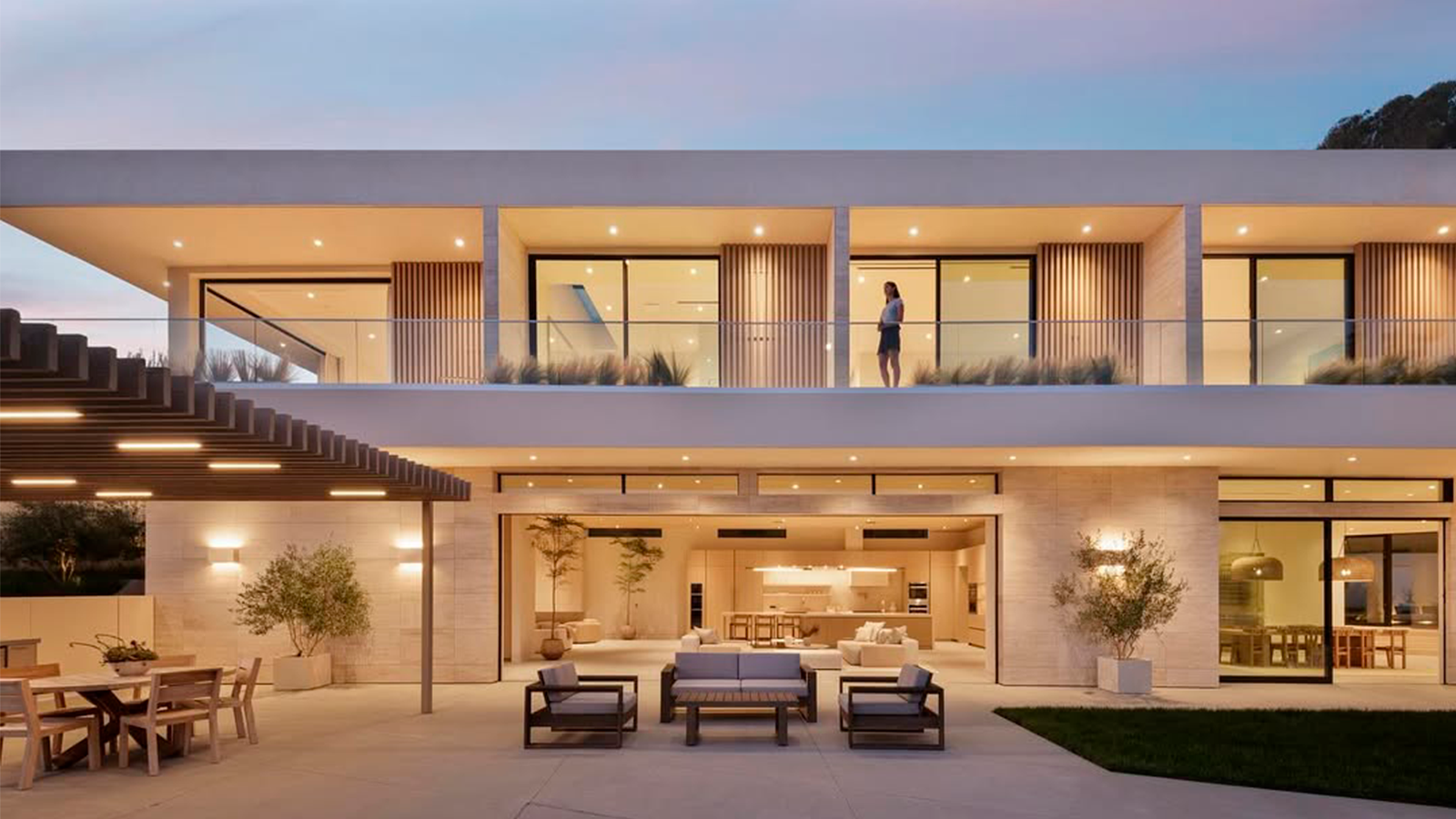 Casa contemporánea de dos pisos al atardecer, con terraza iluminada y living abierto al jardín